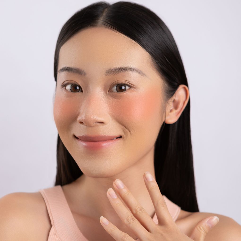 A woman wearing on her cheek Oplenza highly pigmented, bold color dewy Blush Stick in shade Brighten