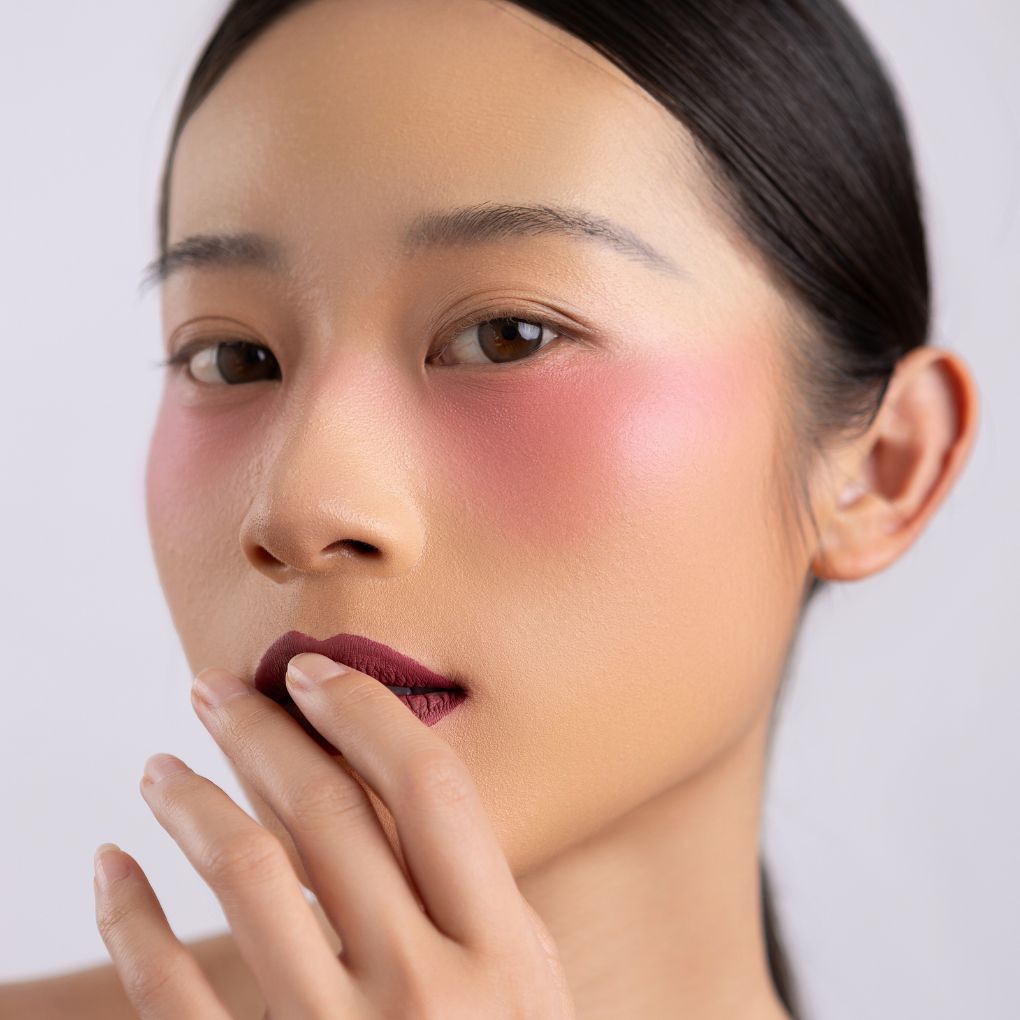 A woman wearing on her cheek Oplenza highly pigmented, bold color dewy Blush Stick in shade Delight