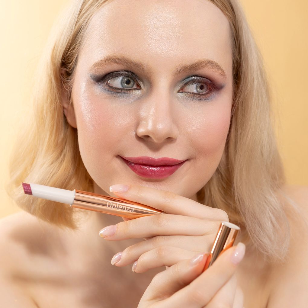 A woman wearing and presenting Oplenza's Hydrating Shimmer Glossy Lip Balm in shade Posh