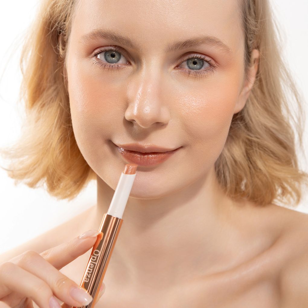 A woman wearing and presenting Oplenza's Hydrating Shimmer Radiant Lip Balm in shade Praline