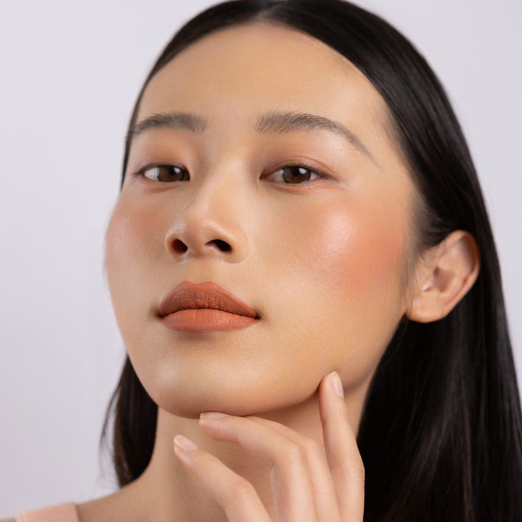 A woman wearing on her cheek Oplenza highly pigmented, bold color dewy Blush Stick in shade Zest
