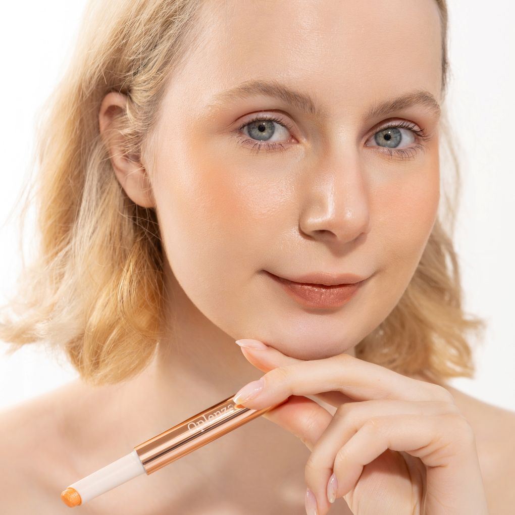A woman wearing and presenting Oplenza's Hydrating Shimmer Luminous Lip Balm in shade Afterglow